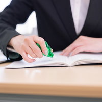 緑色の修正テープで書類を訂正中の女性の手元の写真