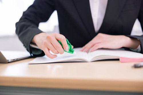緑色の修正テープで書類を訂正中の女性の手元
