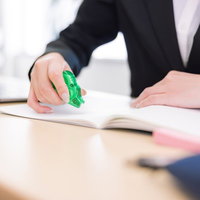 オフィスの机上で書類に修正テープを当てて訂正作業をする女性の手元の写真