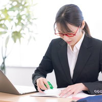 修正テープを握って書類を訂正する女性会社員の写真