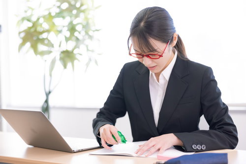 修正テープを握って書類を訂正する女性会社員