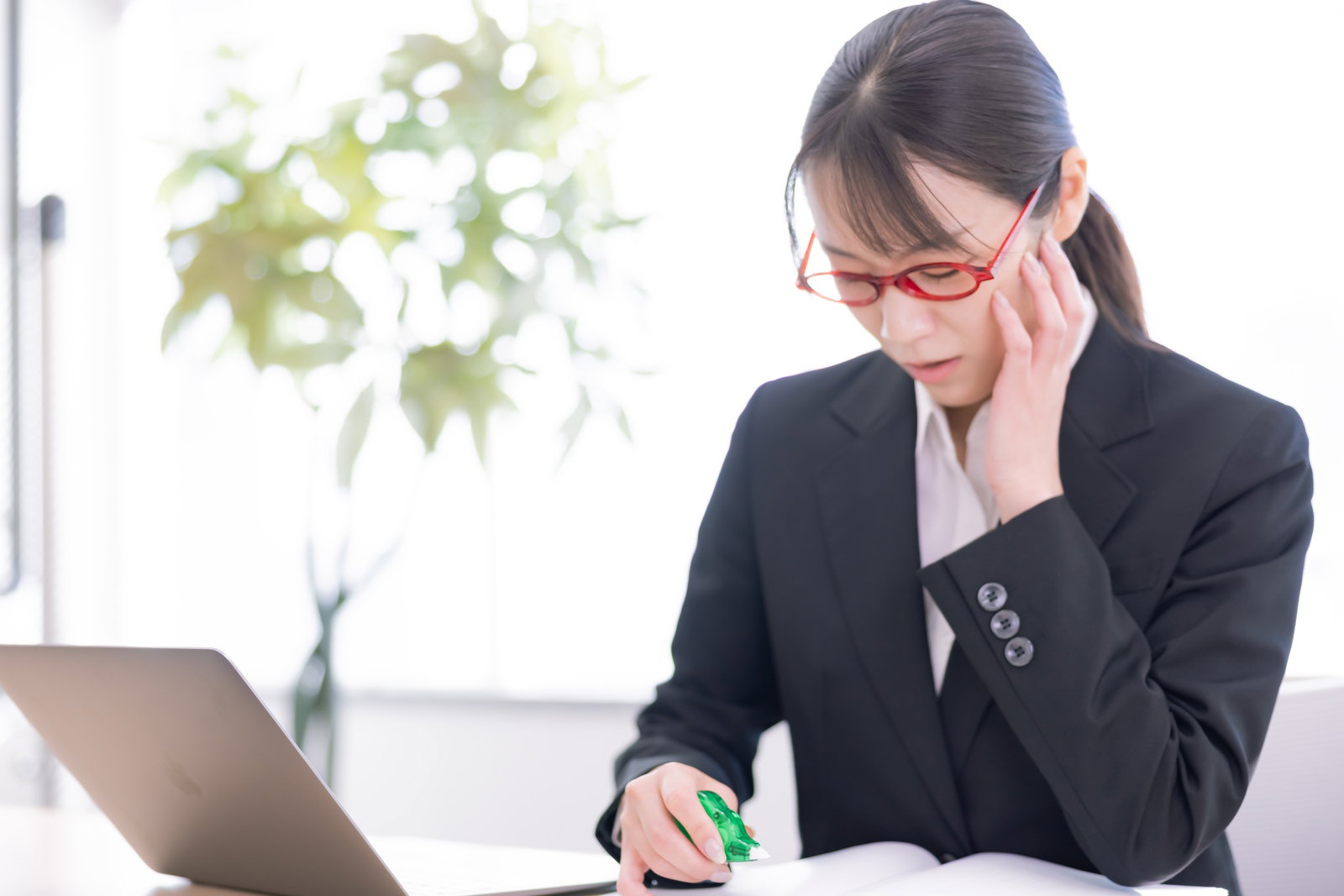 修正テープを持ちながら頭に手を当てる眼鏡をかけた女性［モデル：SAKI］