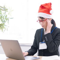 クリスマス時期にサンタ帽をかぶりパソコン業務する女性社員の写真