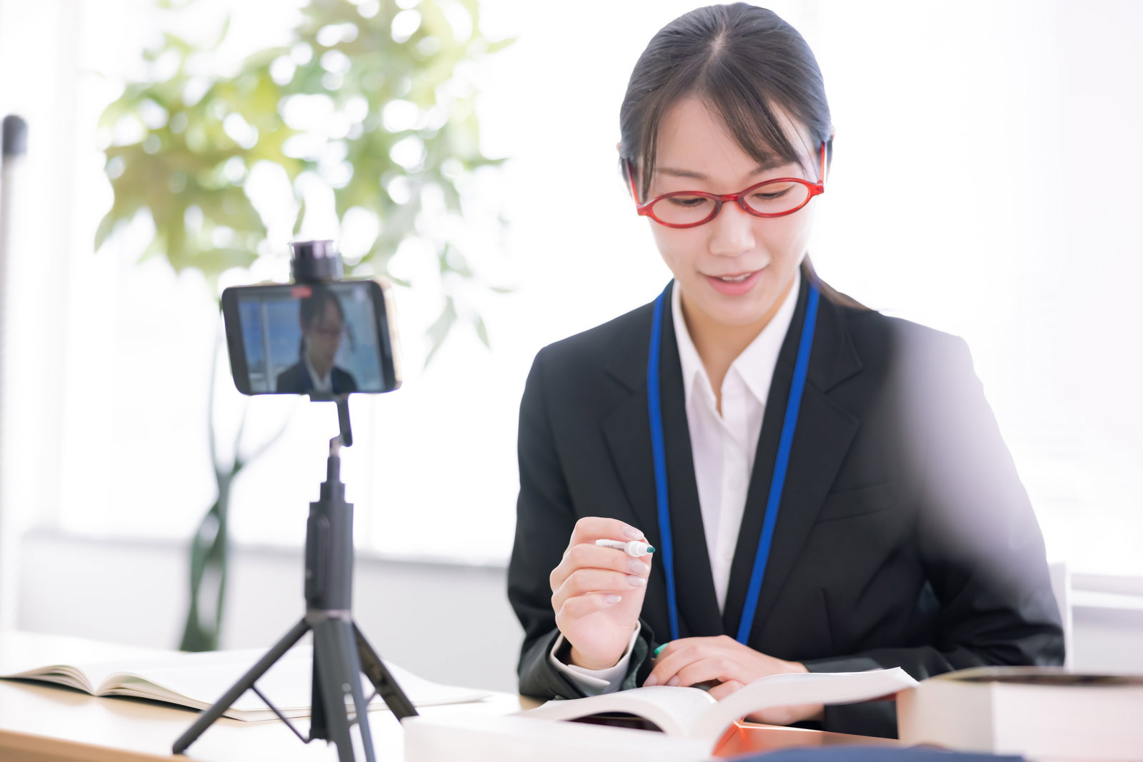 スマートフォンでオンライン会議を行う眼鏡をかけた女性指導員［モデル：SAKI］