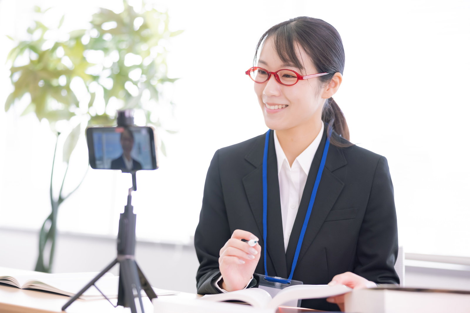 オンライン会議で笑顔を見せるスーツ姿の眼鏡をかけた女性［モデル：SAKI］