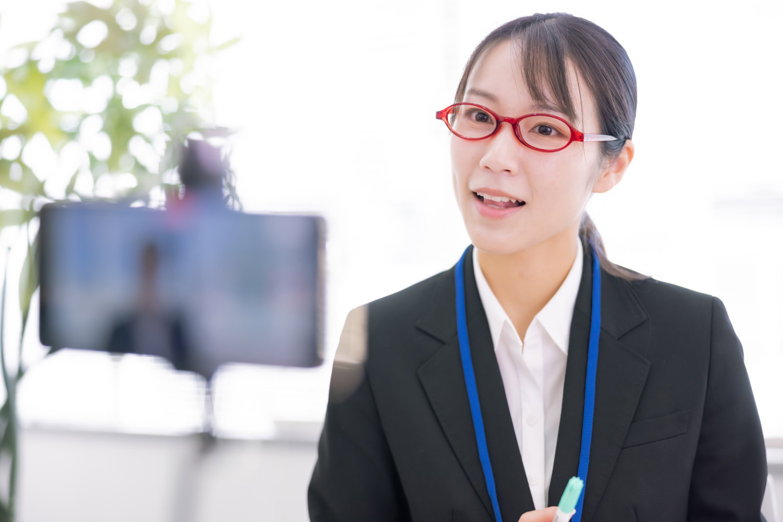 黒いスーツを着た眼鏡の女性がスマホカメラに向かって話している様子［モデル：SAKI］