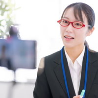 スマホ画面に語り掛ける眼鏡の女性講師によるオンライン会議映像の写真
