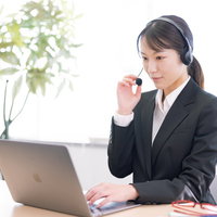 ヘッドセットを装着してノートパソコンで業務中の女性オペレーターの写真