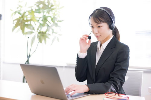 ヘッドセットを装着してノートパソコンで業務中の女性オペレーター