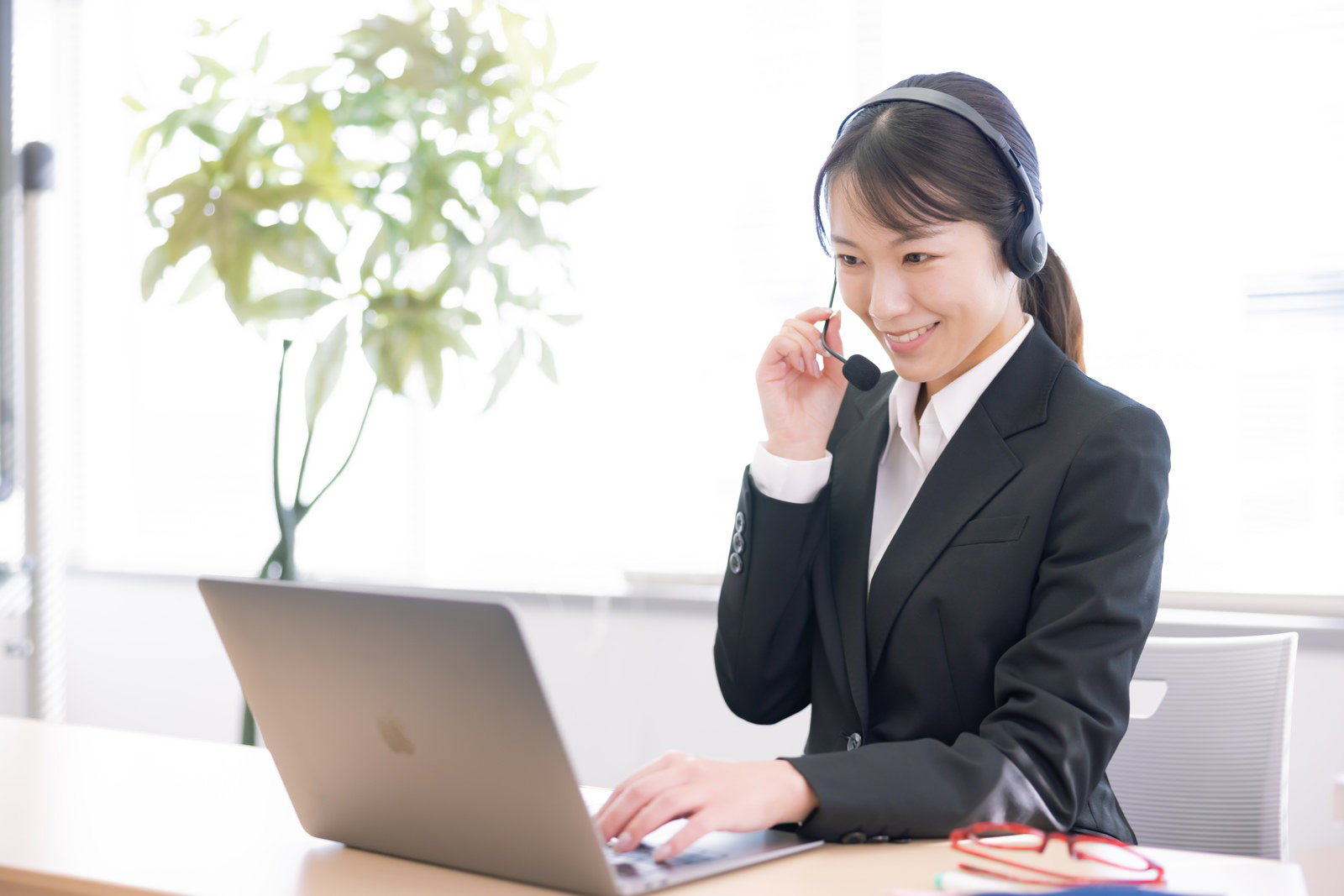 ヘッドセットを着用してパソコンで電話対応をする女性［モデル：SAKI］
