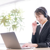 ヘッドセット着用で笑顔でテレアポ業務をこなす女性社員の写真