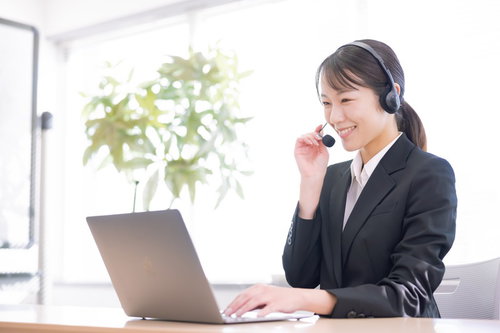 ヘッドセットを着用してパソコンで電話対応をする笑顔の女性オペレーター