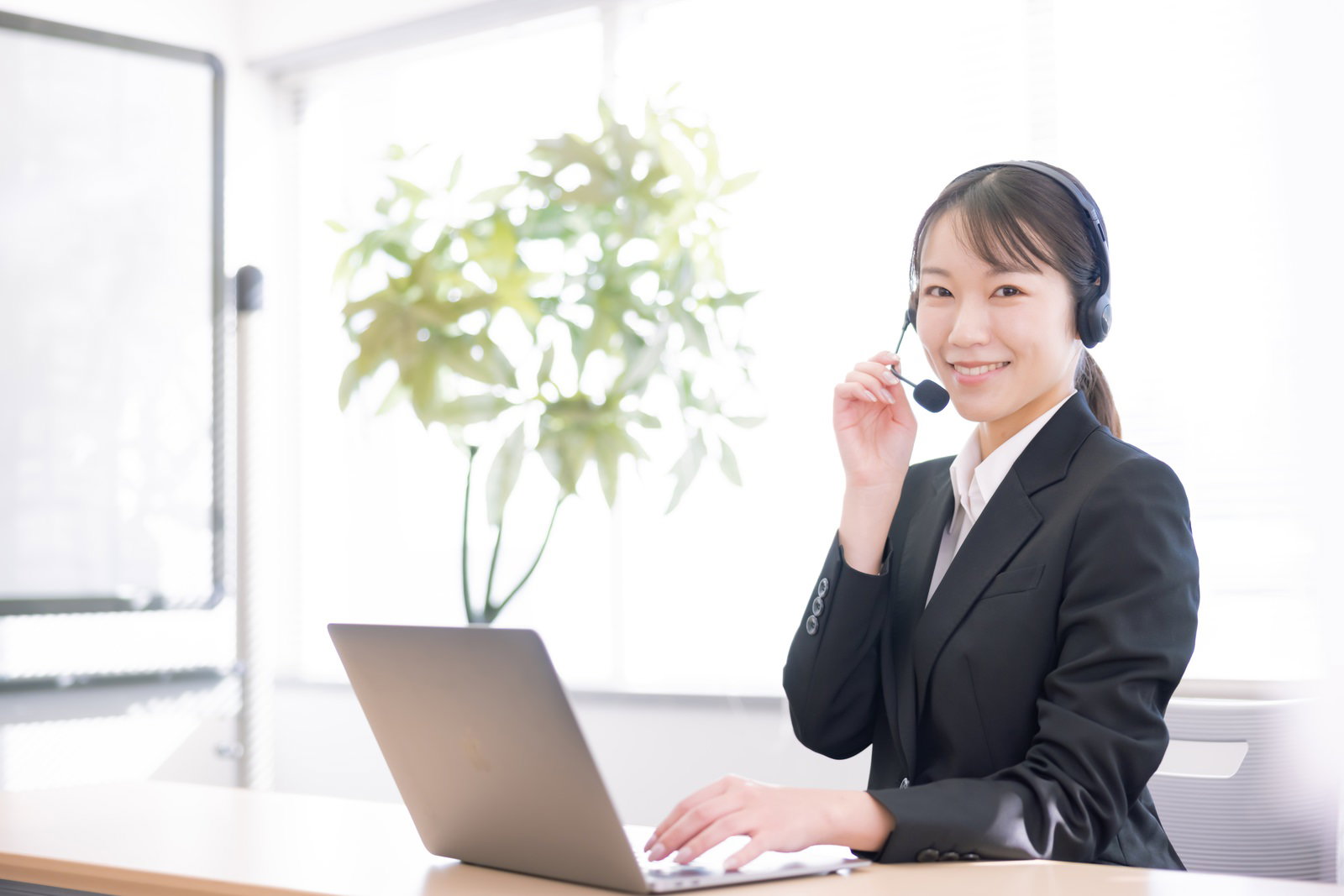 ヘッドセットを装着してマイクに手を添えるスーツ姿の女性［モデル：SAKI］