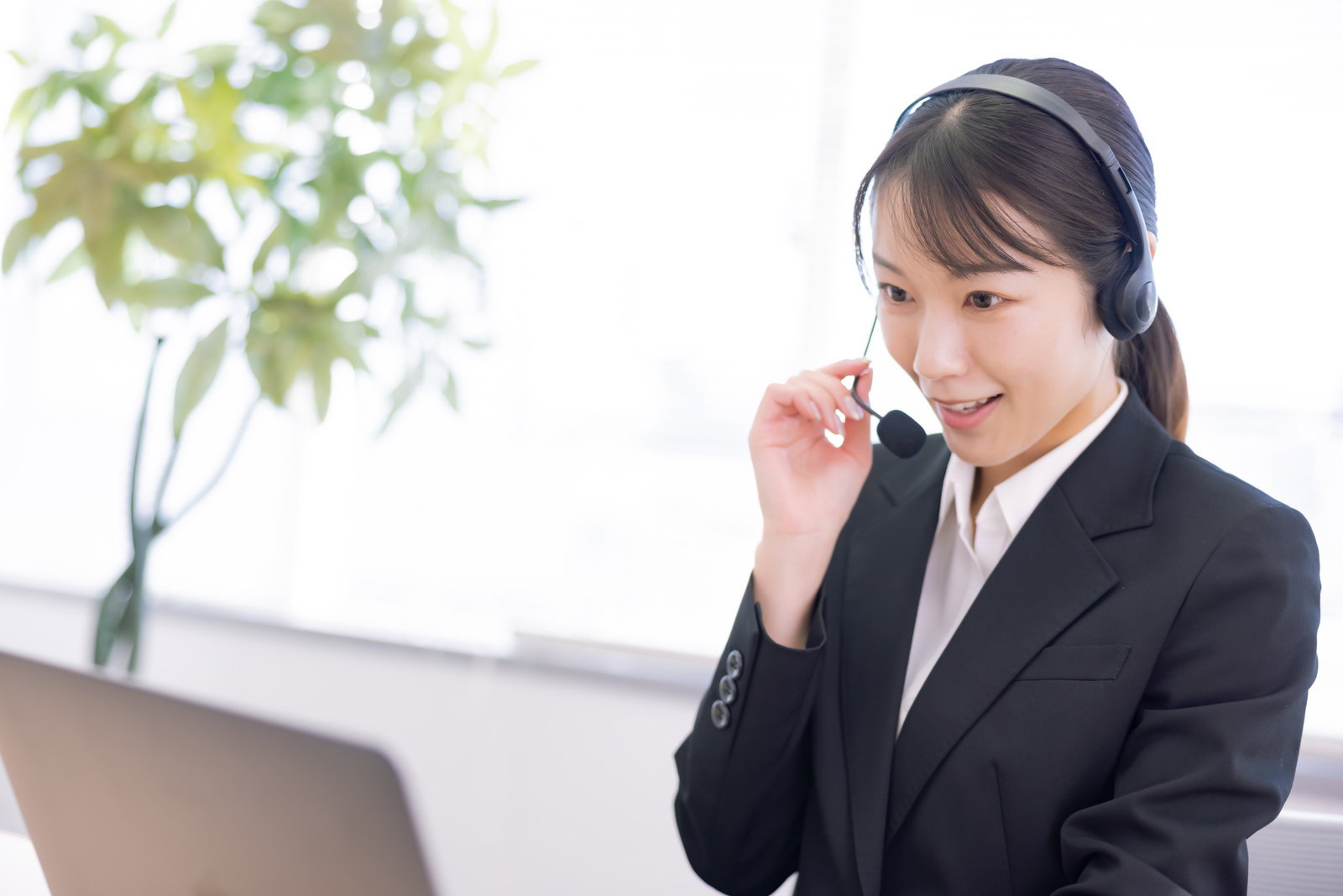 ヘッドセットを装着してマイクに向かって話すコールセンターの女性オペレーター［モデル：SAKI］