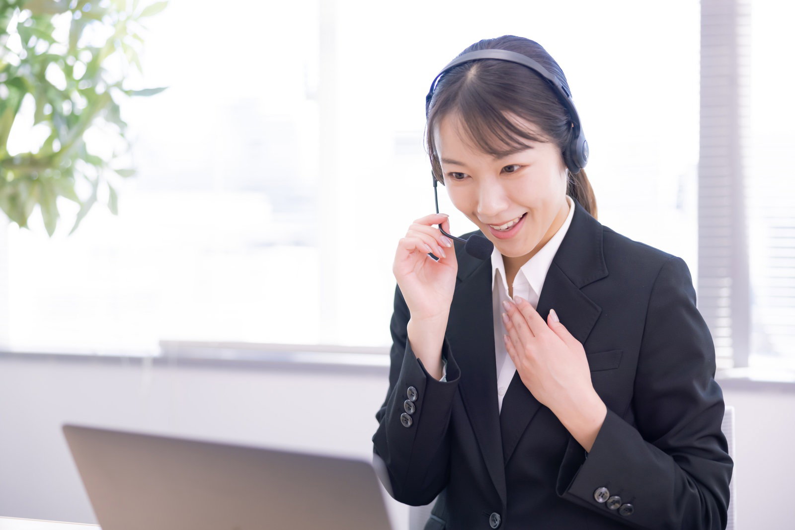 オフィスでマイクを調整しながら電話対応する女性オペレーター［モデル：SAKI］