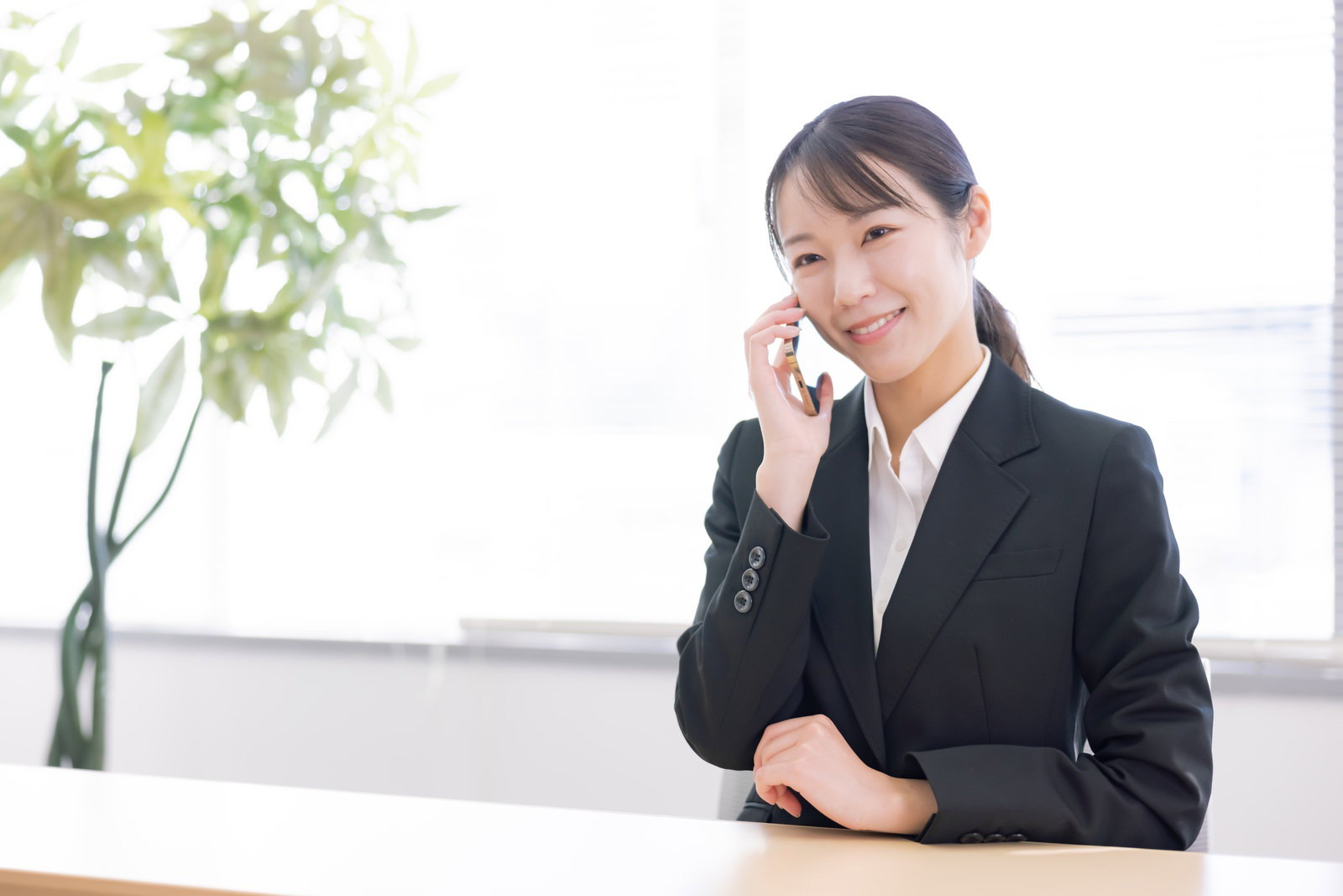 黒いスーツを着て微笑みながら電話をしている女性事務員