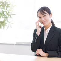 黒いスーツで微笑みながら通話中の女性事務員の写真