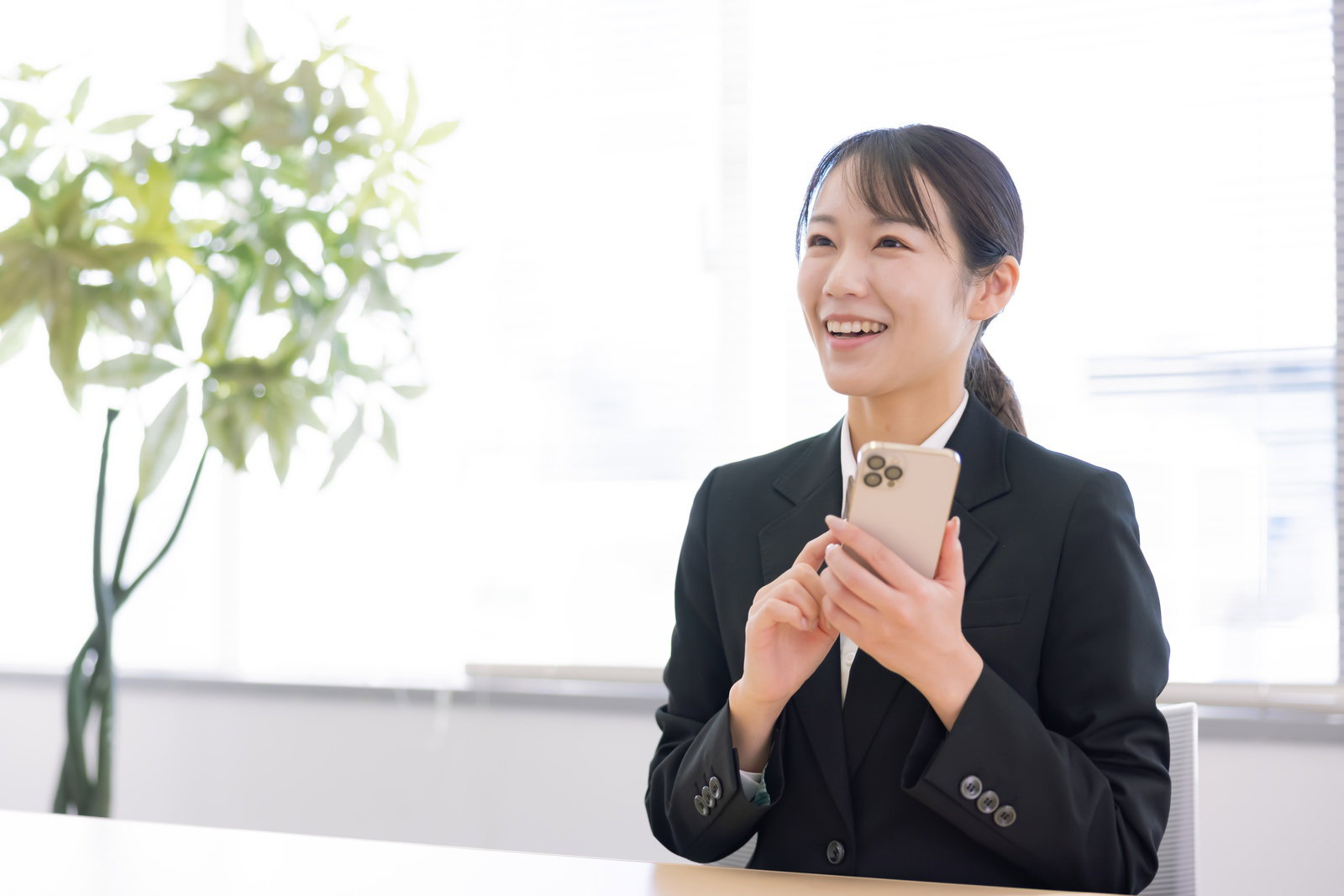 スマートフォンを持ち笑顔で見つめる新入社員の女性［モデル：SAKI］