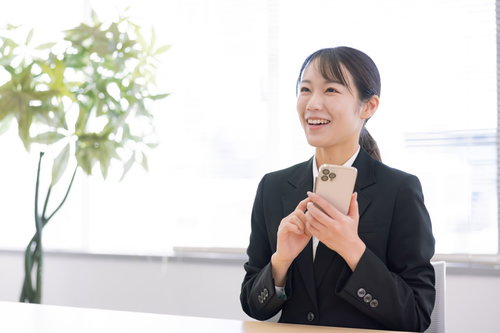 スマホを手に笑顔で見つめる新入社員の女性