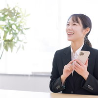 スマートフォンを手に取る女性事務員の笑顔の写真