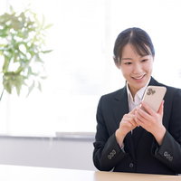 笑顔でスマートフォンを操作する新入社員女性の写真