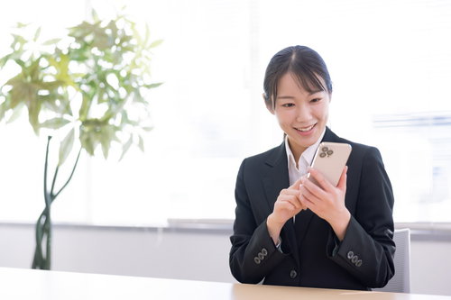 笑顔でスマートフォンを操作する新入社員女性