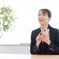 黒いスーツを着てスマホを手に持ち笑顔の女性の写真