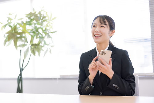 黒いスーツを着てスマホを手に持ち笑顔の女性
