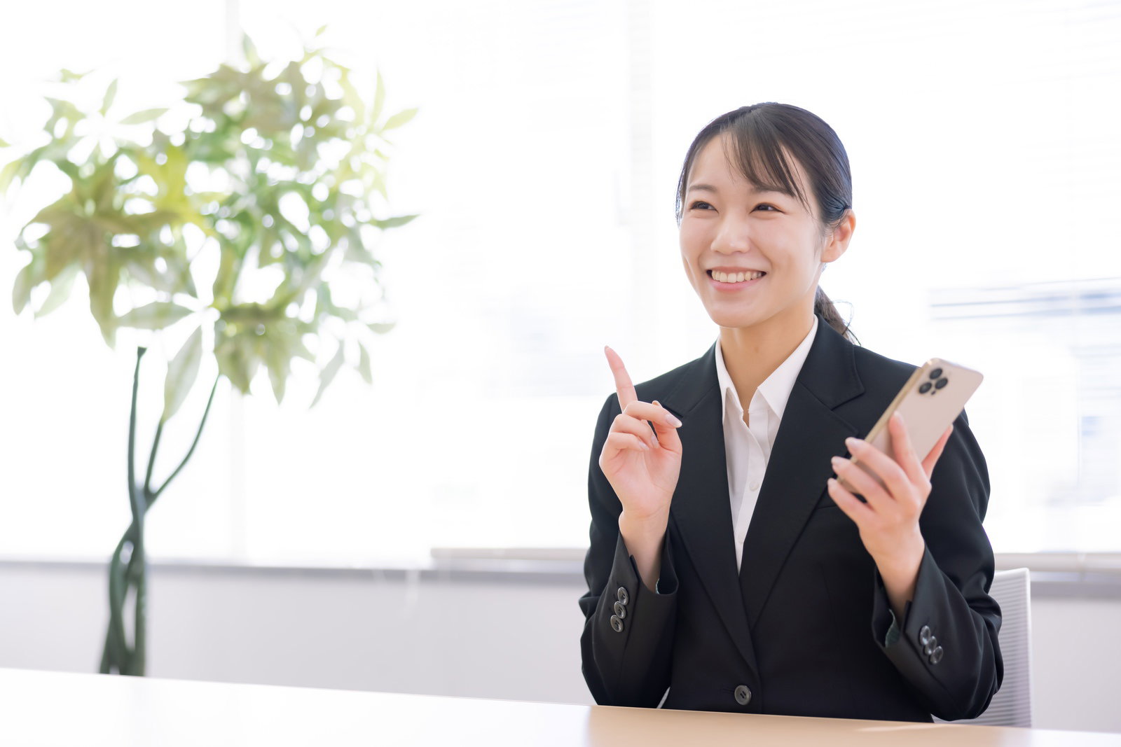 スマートフォンを持ちながら人差し指を立てて笑う女性［モデル：SAKI］