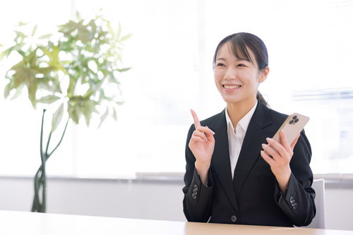 スマホを持ちながら笑顔で人指し指を立てる女性