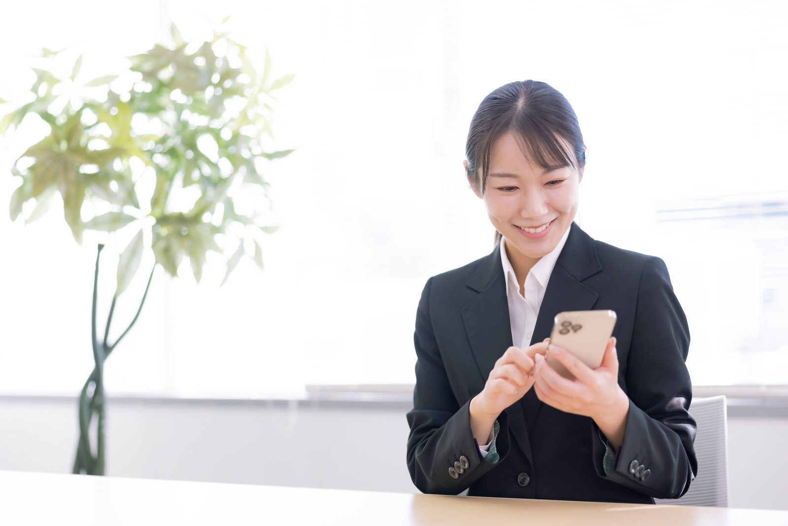 スマートフォンを両手で持ち、笑顔で画面を見つめながら操作する黒いジャケット姿の女性［モデル：SAKI］