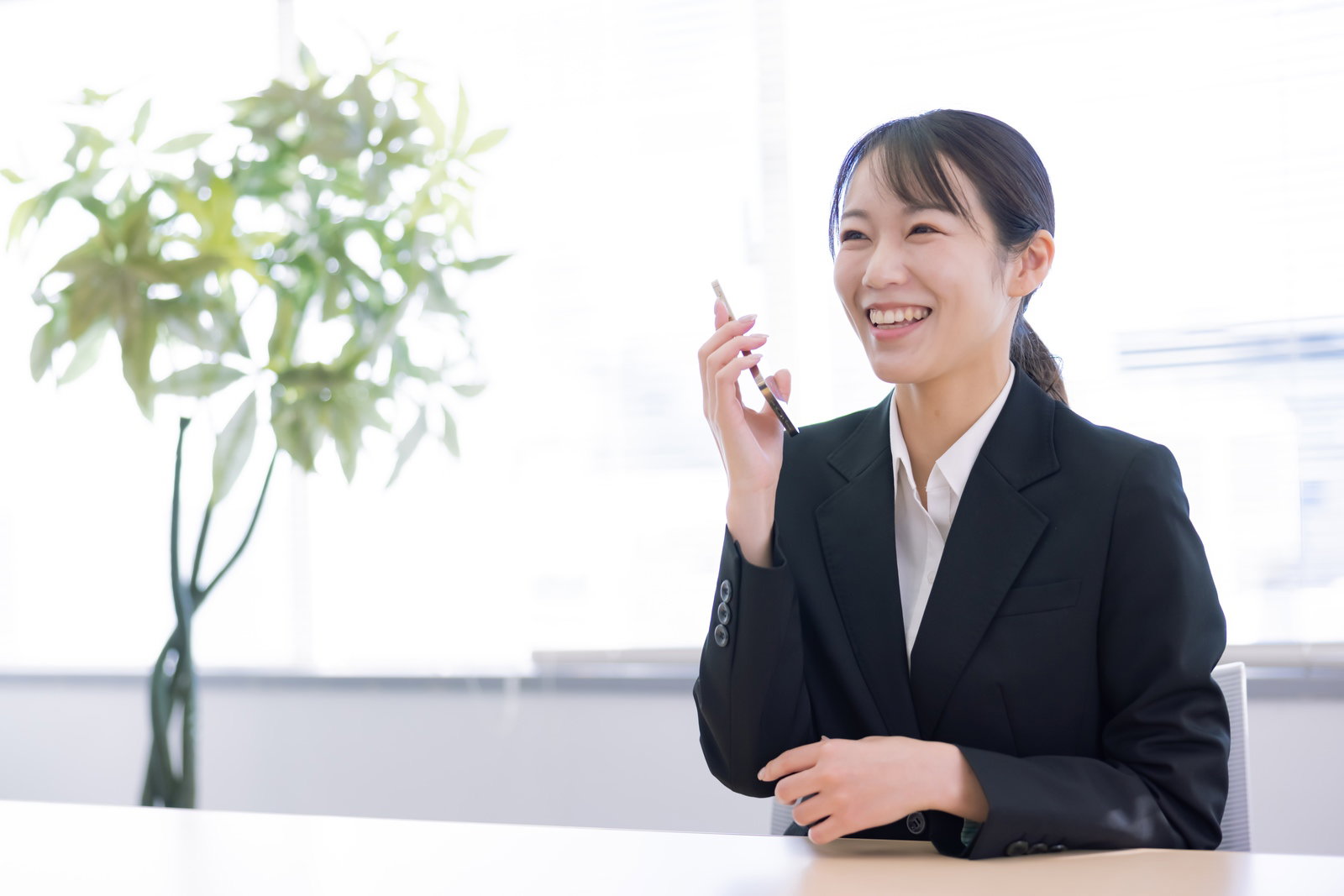 黒いスーツを着た女性がスマートフォンで通話している様子［モデル：SAKI］