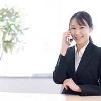 スマホで笑顔で電話相談中の女性オフィスワーカーの写真