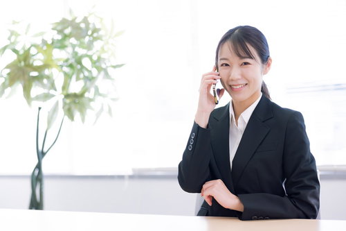 スマホで笑顔で電話相談中の女性オフィスワーカー