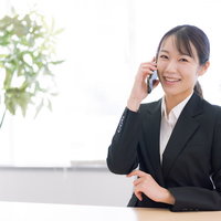 黒いスーツで電話対応中に微笑む女性会社員の写真