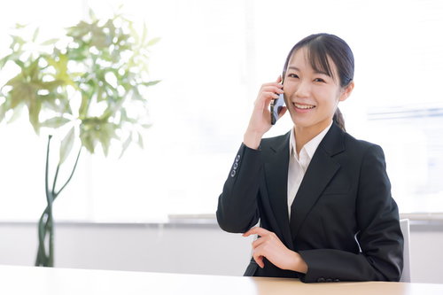 黒いスーツで電話対応中に微笑む女性会社員