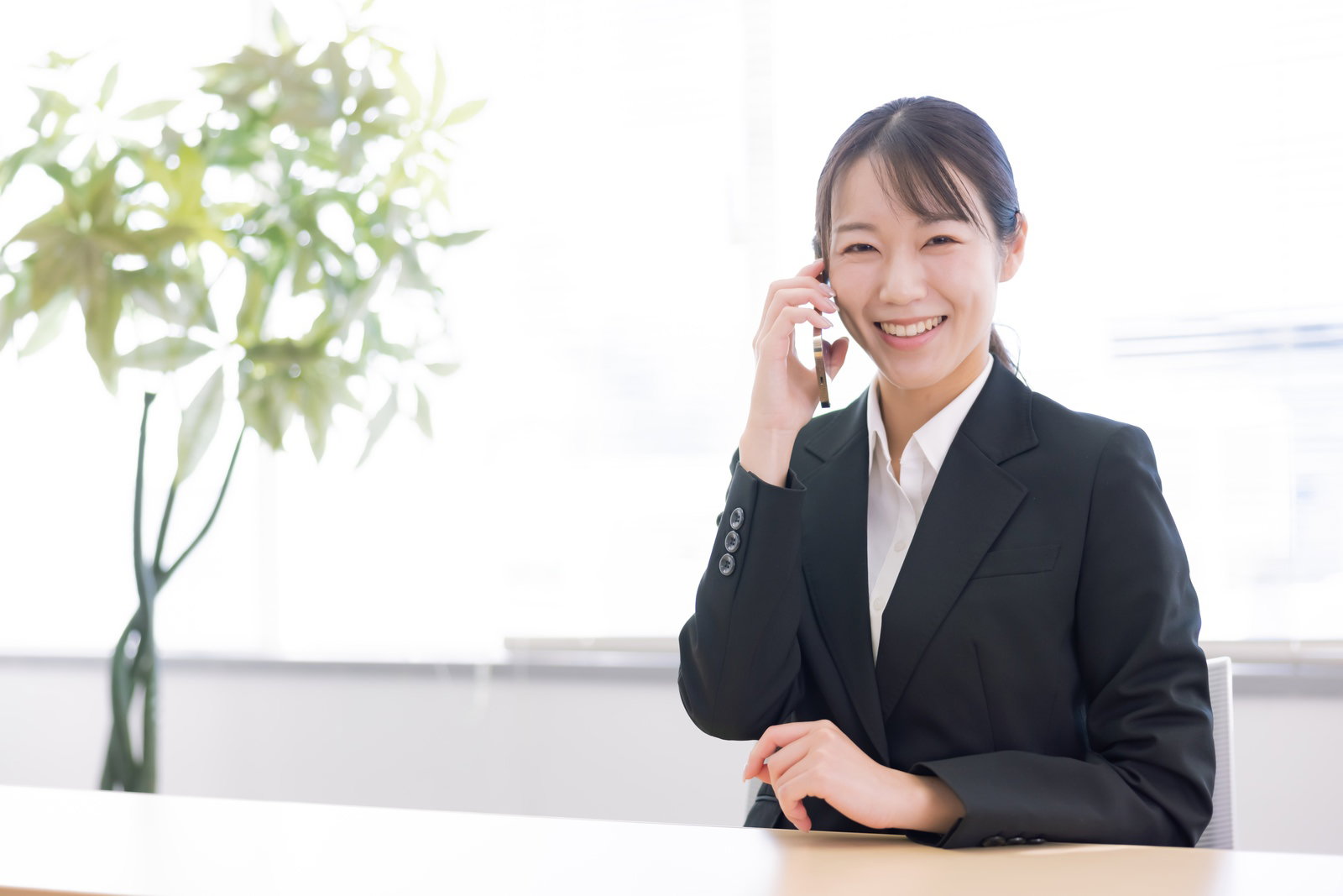 黒いスーツを着た女性事務員がスマートフォンで通話している様子［モデル：SAKI］