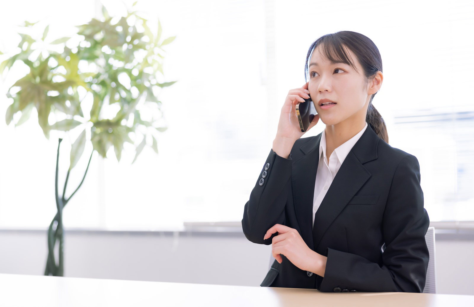 深刻な表情でスマートフォンで通話するスーツ姿の女性［モデル：SAKI］
