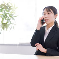 深刻な表情でスマホで通話するスーツ姿の女性の写真