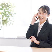 スマートフォンで通話しながら微笑む黒いスーツの女性の写真