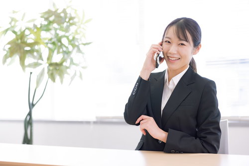 スマートフォンで通話しながら微笑む黒いスーツの女性