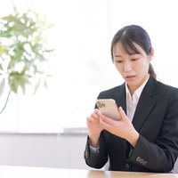スマホ操作に困惑する女性会社員の写真