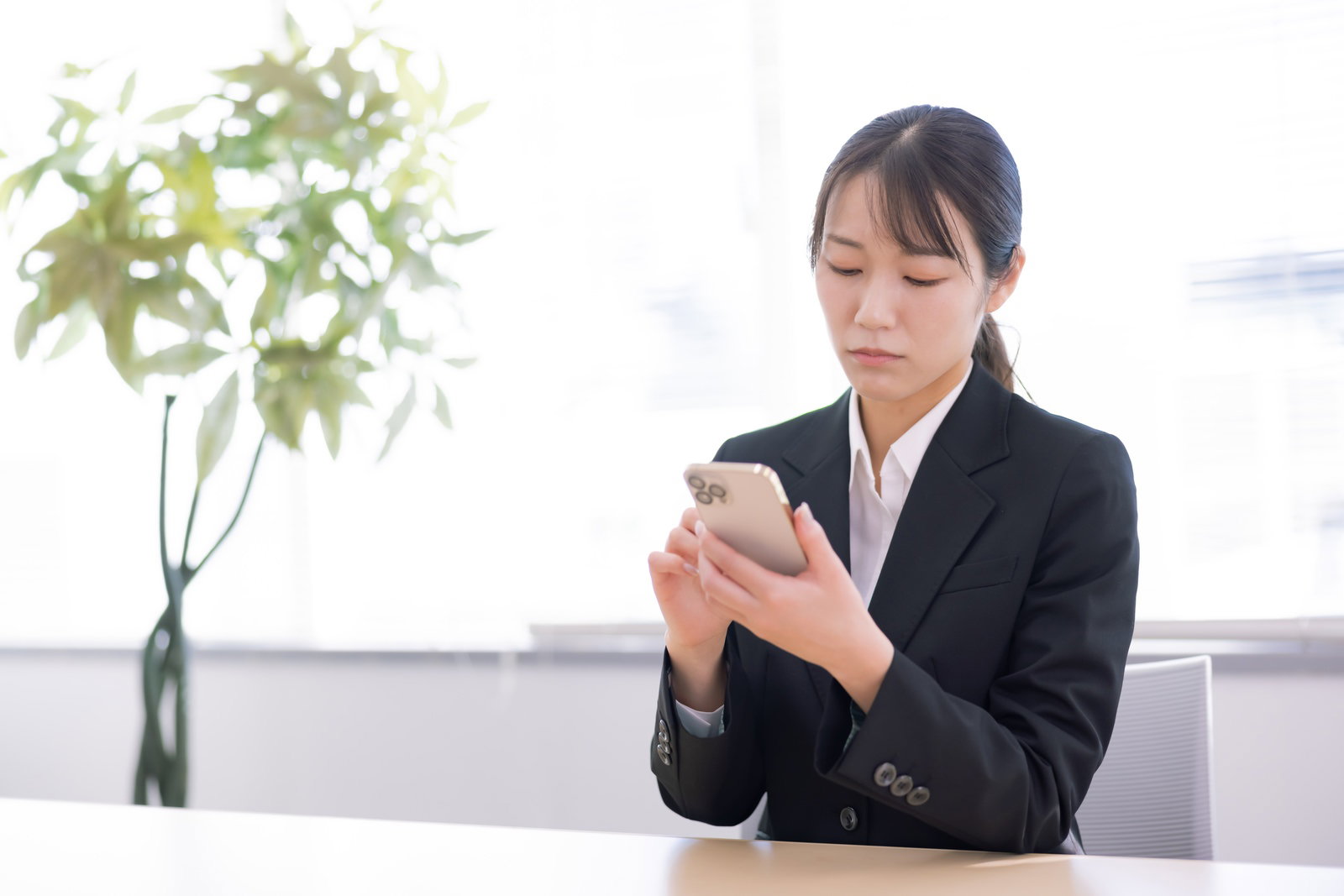 オフィスのデスクでスマホを見て困惑する女性［モデル：SAKI］