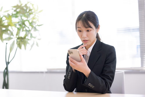 黒スーツでスマートフォンを見て驚く女性事務員
