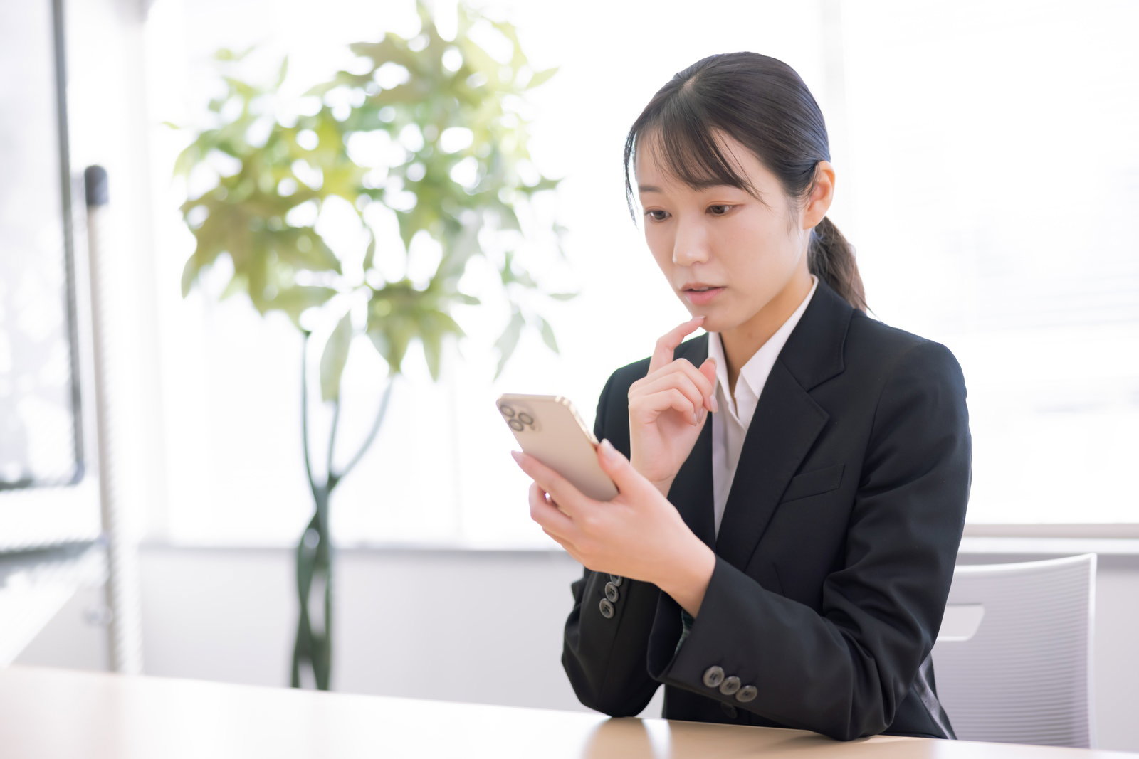 スマホを見て首をかしげながら考える女性事務員［モデル：SAKI］