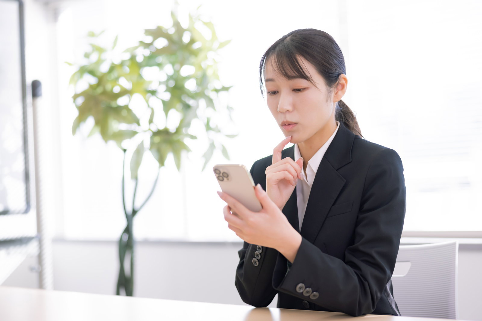 A woman in a black suit looking troubled as she ponders her smartphone