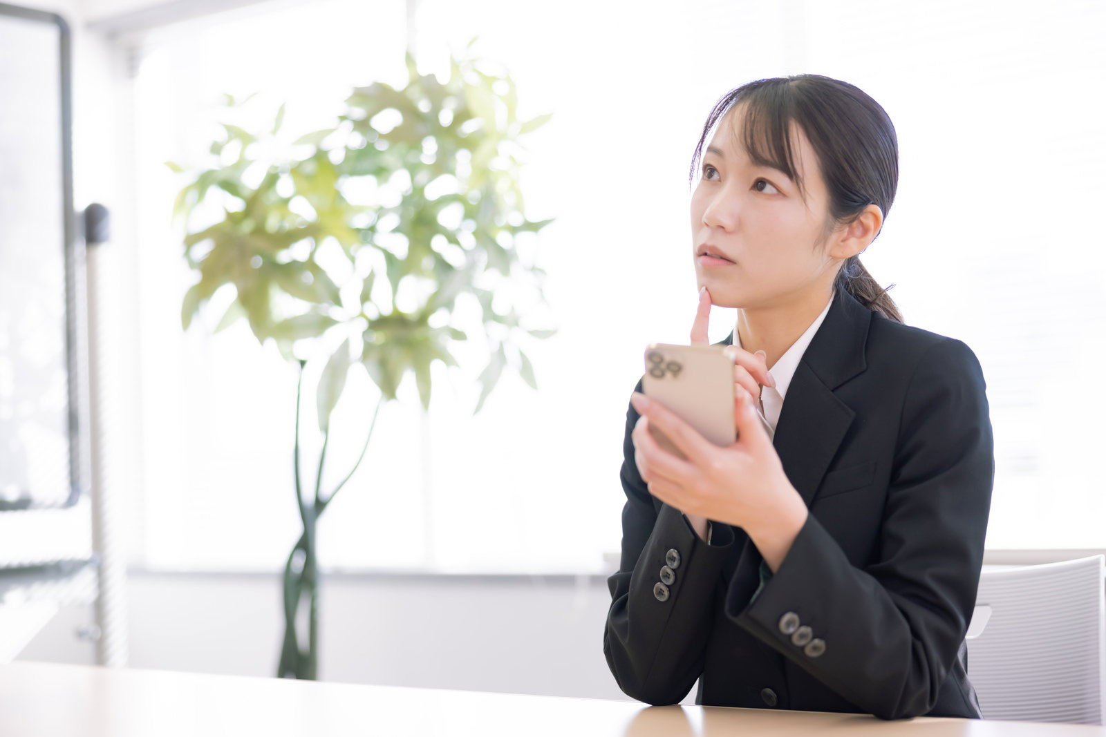 A woman in a black suit looking confused while looking at a smartphone
