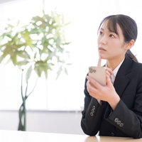 スマホ片手に困惑する黒いスーツの会社員女性の写真