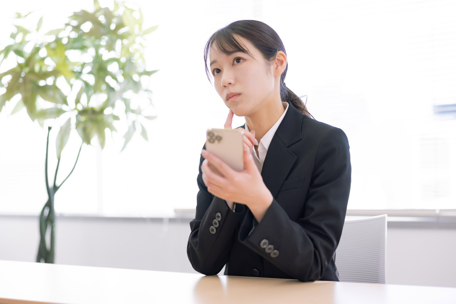 Woman in black suit looking confused while examining her smartphone in an office setting