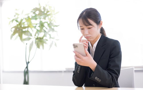 黒いスーツを着てスマートフォン画面を見つめる女性